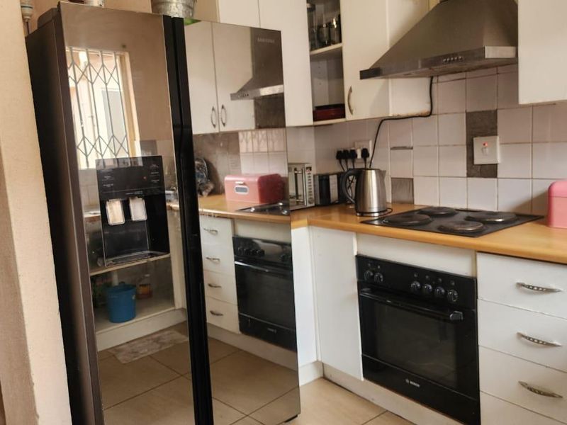 A functional kitchen featuring white cabinetry, a built-in oven with electric hob, extractor fan, and tiled backsplash with laminate countertops.