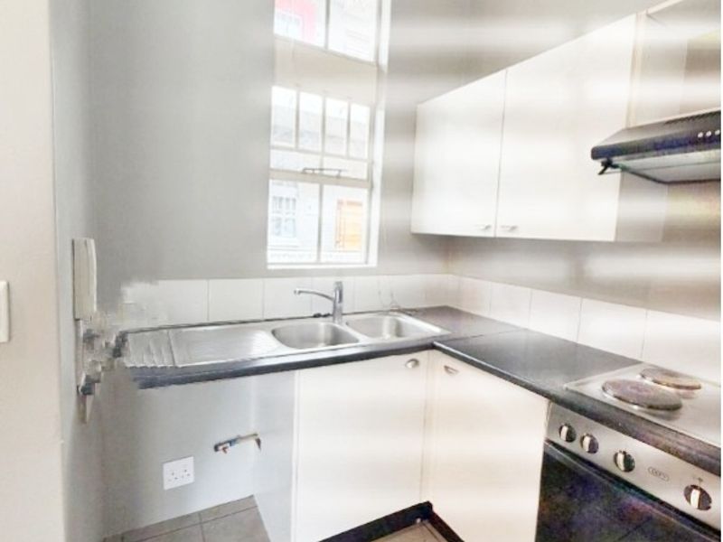 A compact kitchen featuring built-in cabinetry, a stainless steel sink, an electric stove with extractor fan, and tiled flooring.