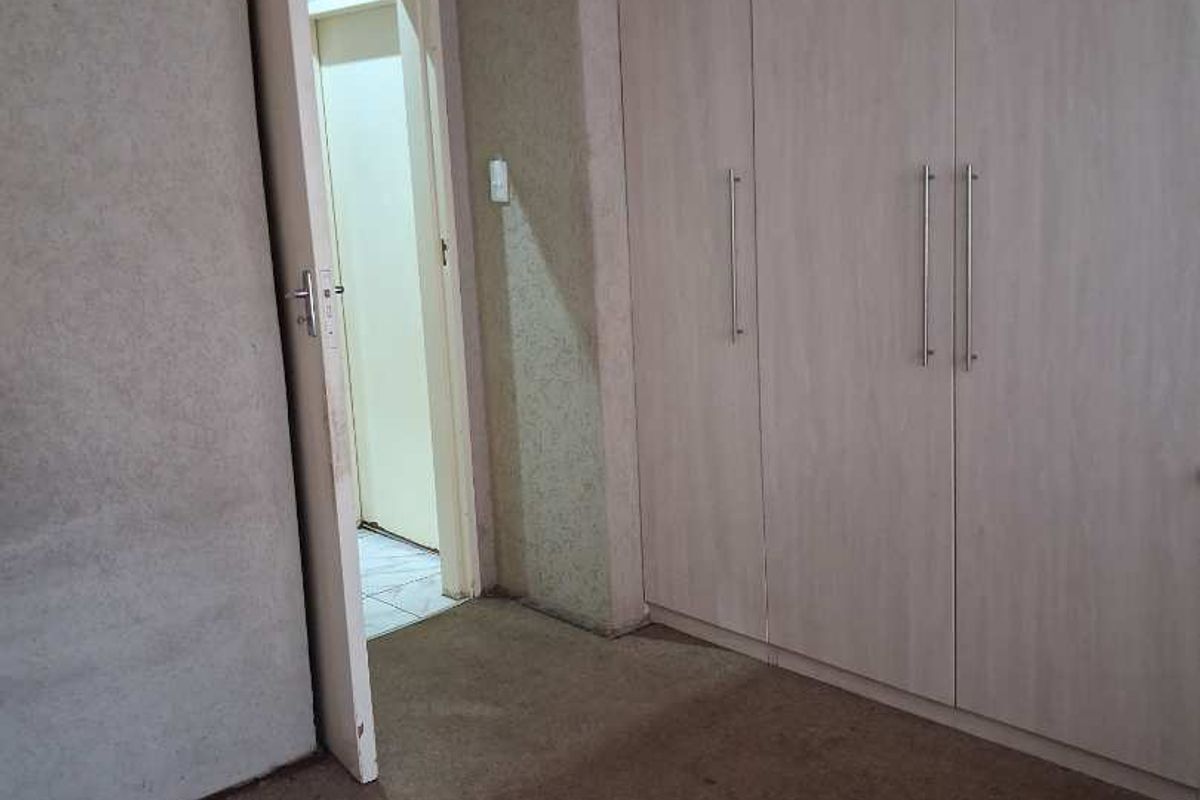 A bedroom featuring built-in wooden cabinetry and carpeted flooring, with an open doorway leading to an adjacent room.