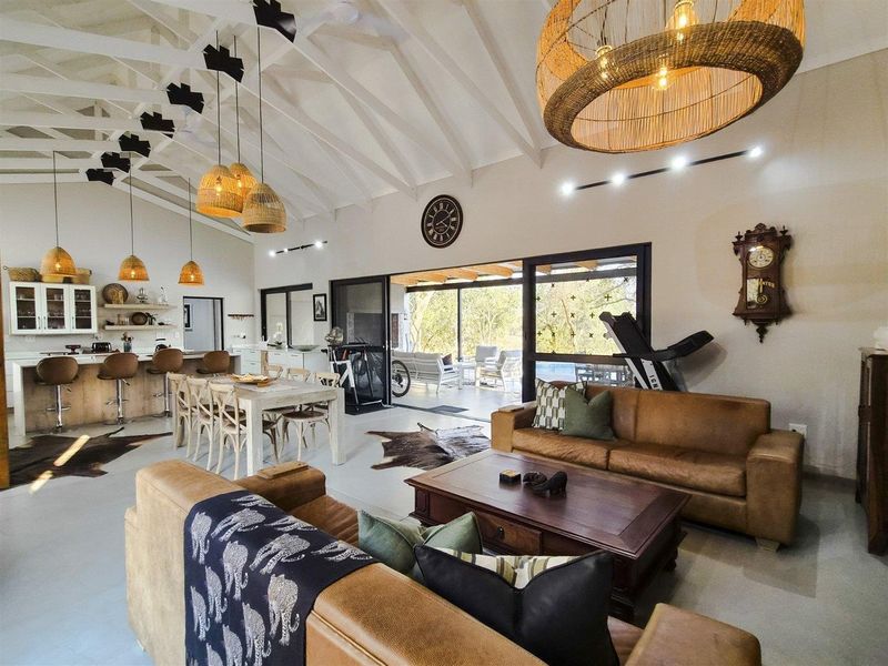 Spacious open-plan living area featuring a vaulted ceiling with exposed rafters, polished concrete floors, and seamless flow to the outdoor patio through sliding doors.