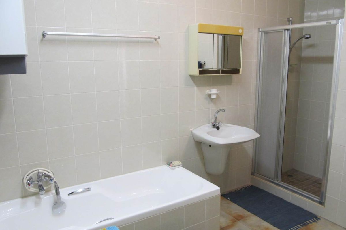 A functional bathroom featuring a built-in bathtub, a separate glass-enclosed shower, a wall-mounted basin, and a mirrored medicine cabinet with full-height wall tiling.
