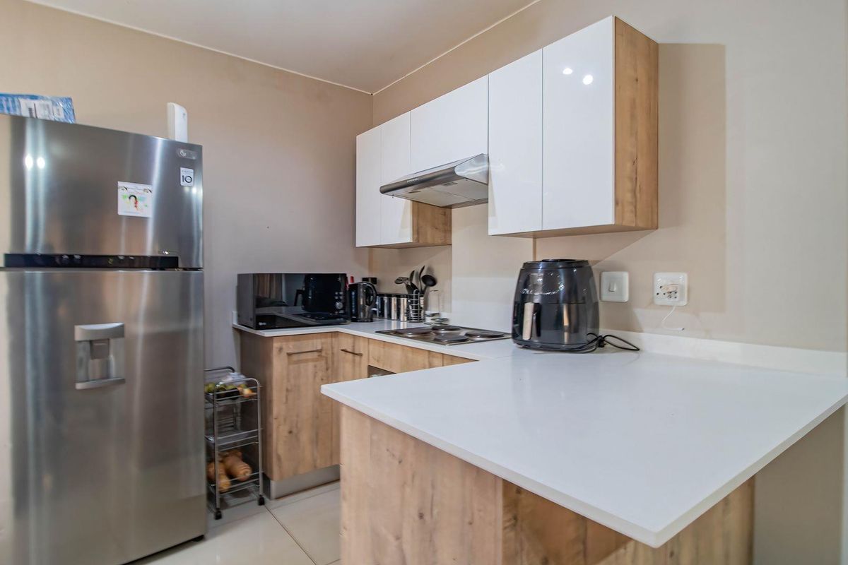 Modern kitchen featuring wood-finish cabinetry, white stone countertops, a built-in hob, and an extractor fan, offering a clean and functional workspace.