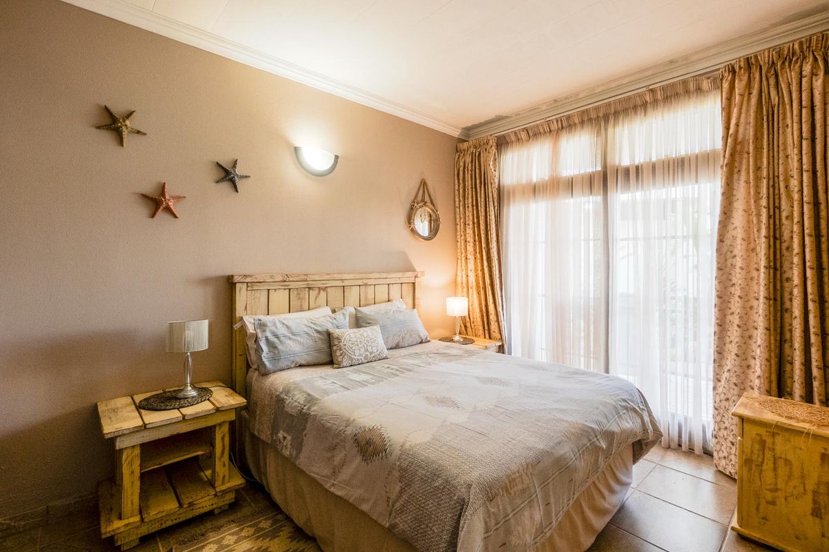 A cozy bedroom featuring tiled flooring, a large window with floor-to-ceiling curtains, and a wall-mounted light fixture.