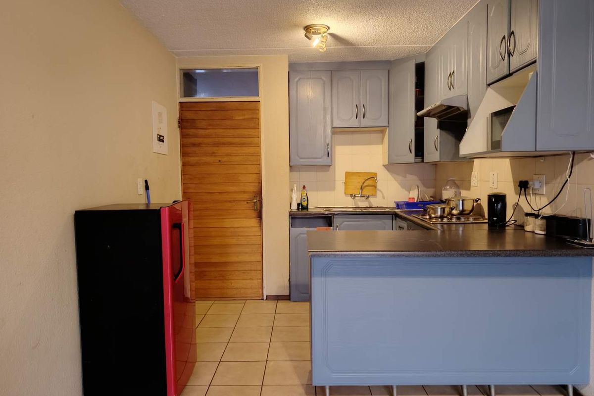 A functional kitchen featuring blue built-in cabinetry, laminate countertops, a stainless steel sink, and tiled flooring, providing a practical workspace for daily needs.