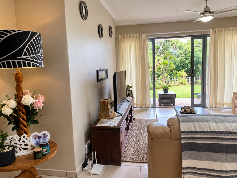 A comfortable living room featuring tiled flooring, a ceiling fan, and large sliding glass doors that provide direct access to the rear garden.