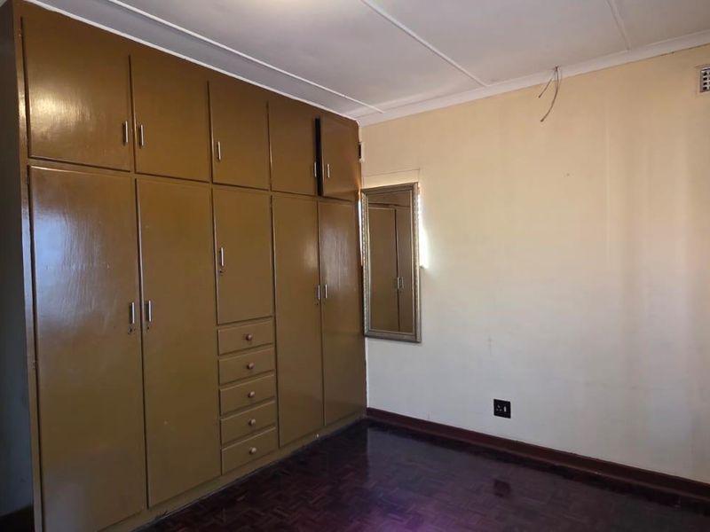 A bedroom featuring dark wood parquet flooring and extensive built-in cupboards, requiring minor cosmetic updates and electrical finishing.