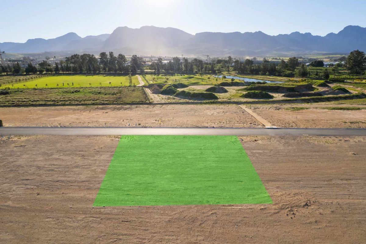 Aerial view of a vacant residential plot featuring a highlighted boundary, paved road access, and scenic mountain views in the background.