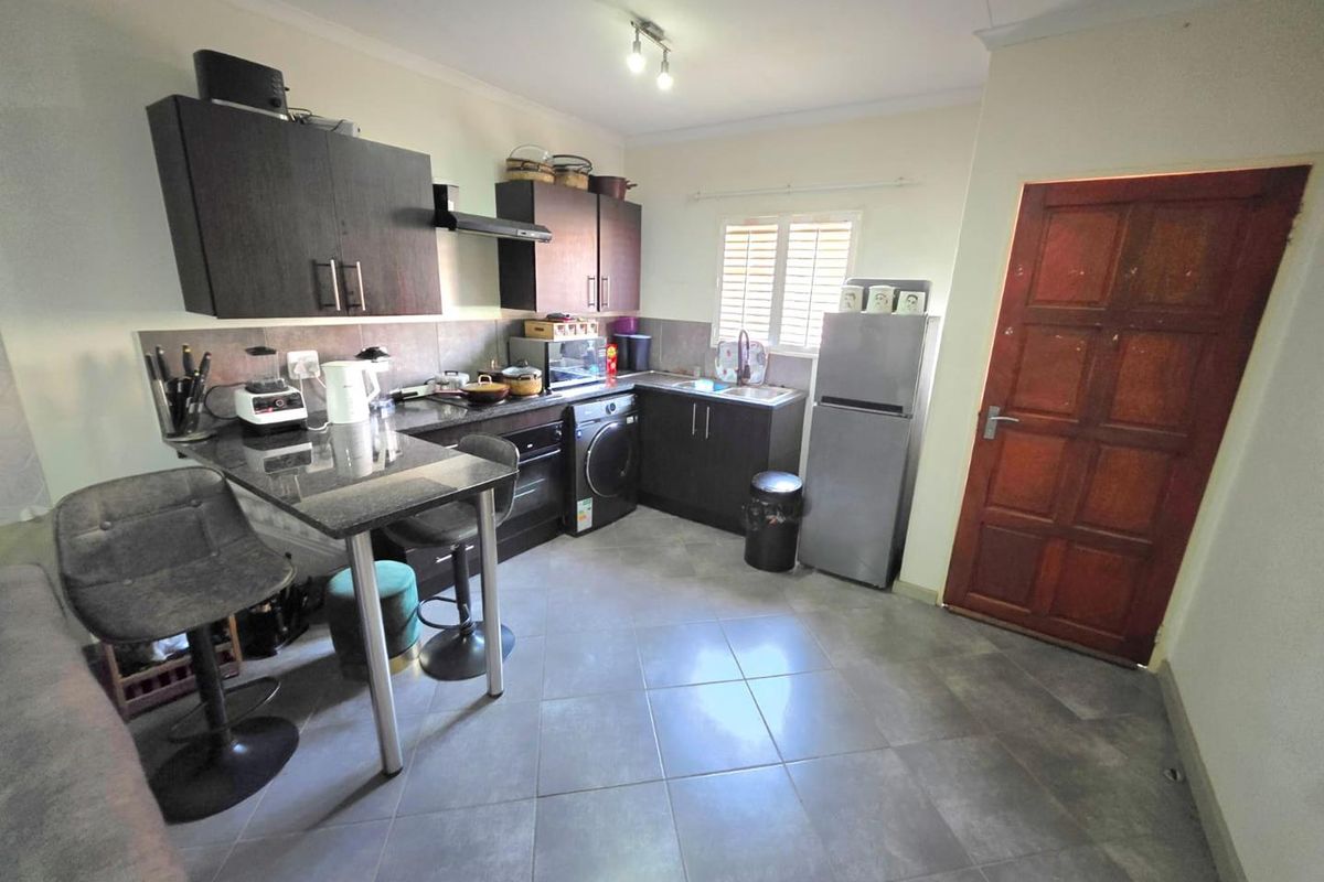 A functional kitchen featuring dark wood cabinetry, granite countertops, tiled flooring, and a direct access timber door.