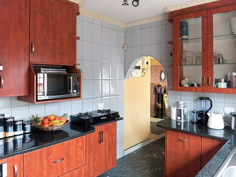 A functional kitchen featuring warm-toned wooden cabinetry, dark granite countertops, a tiled backsplash, and a distinctive arched doorway leading to an adjacent space.