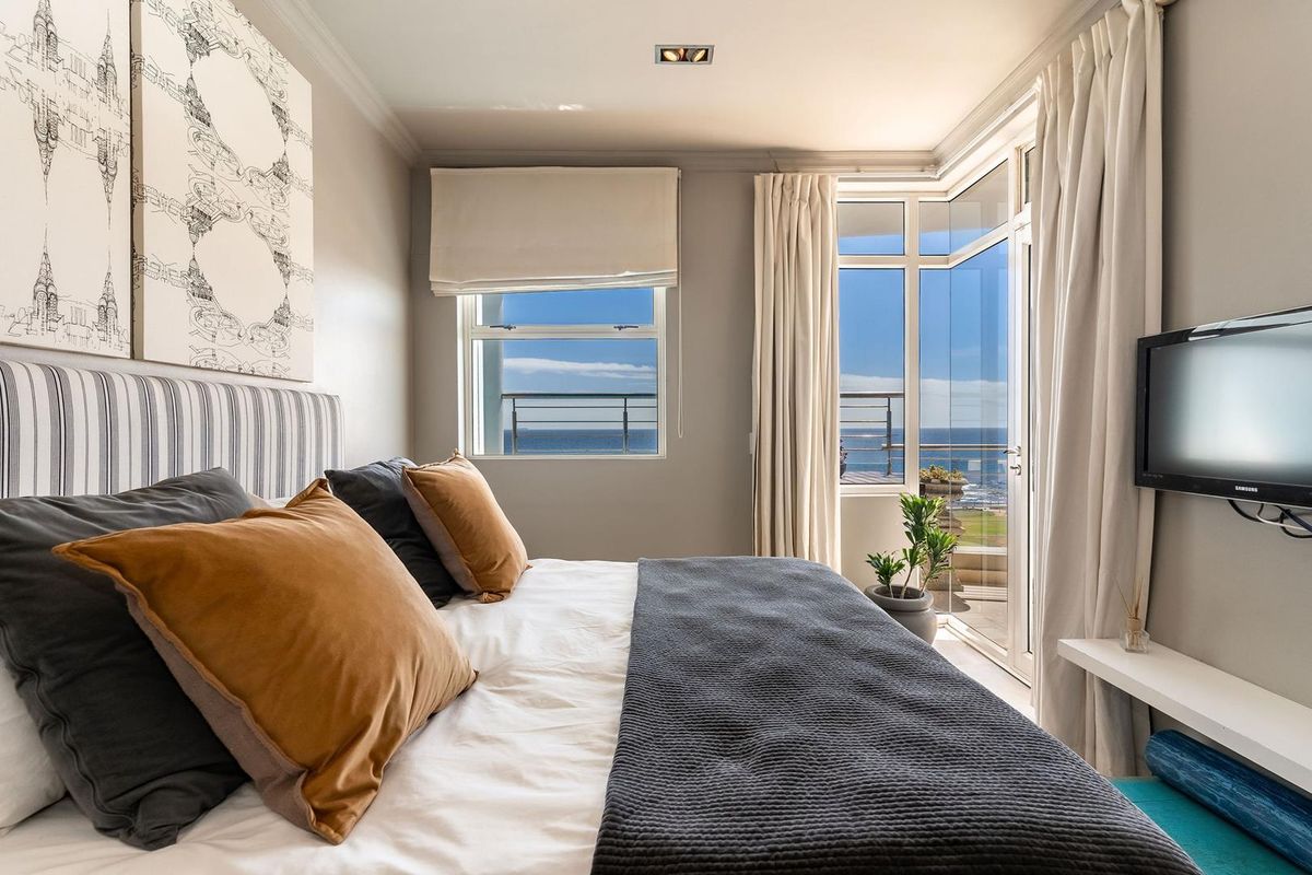 Bright bedroom featuring large windows and a glass door leading to a balcony with scenic ocean views.
