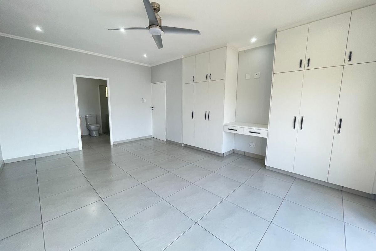 Spacious bedroom featuring neutral tiled flooring, extensive built-in cabinetry with an integrated desk, ceiling fan, and direct access to an en-suite bathroom.
