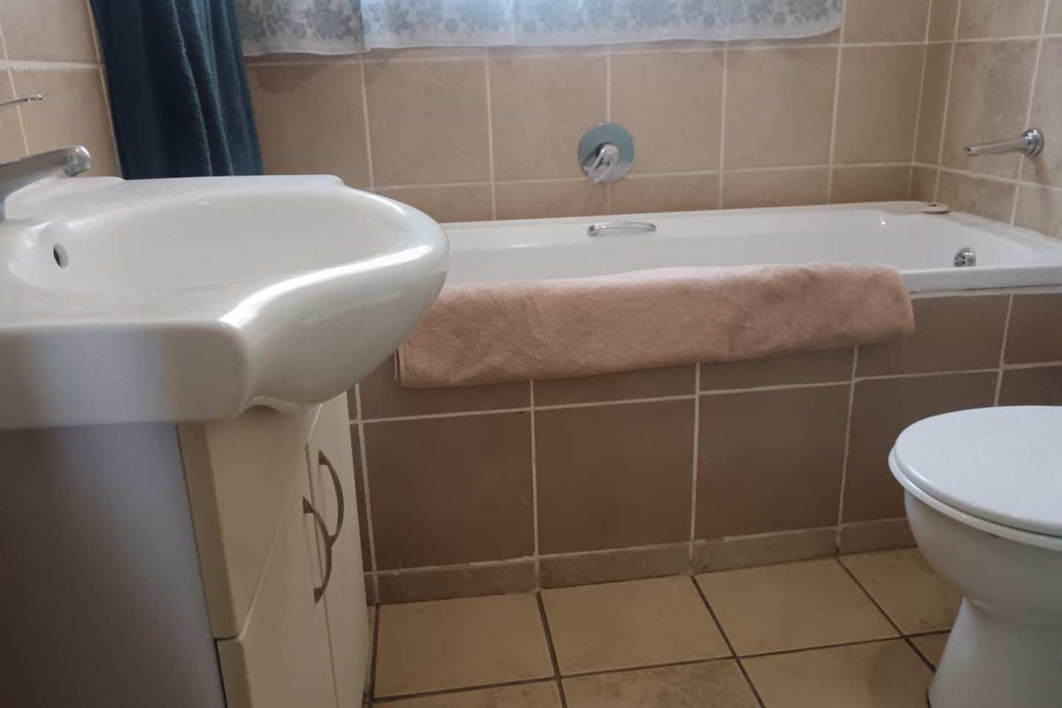 A functional bathroom featuring a built-in vanity with basin, a standard bathtub, and a toilet, finished with neutral wall and floor tiling.