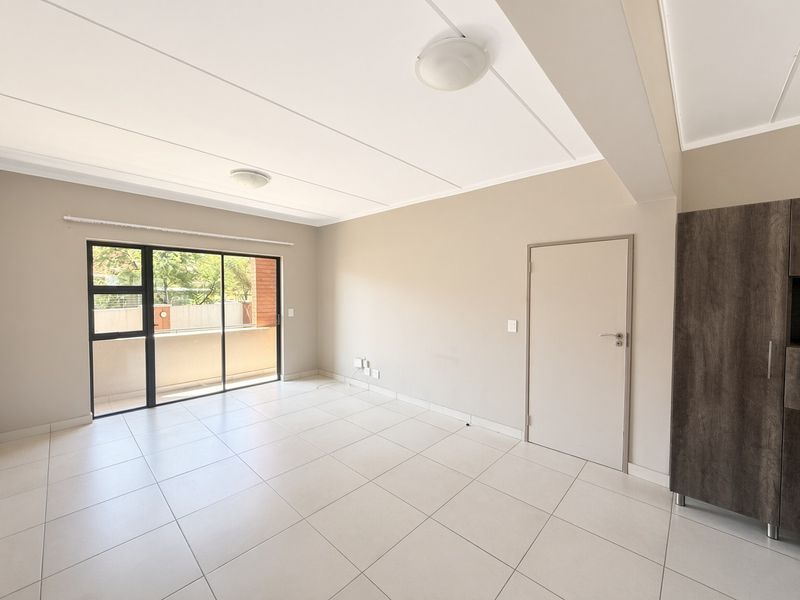 Spacious, light-filled living area featuring neutral tiled flooring, a sliding glass door leading to a balcony, and a built-in storage cupboard.