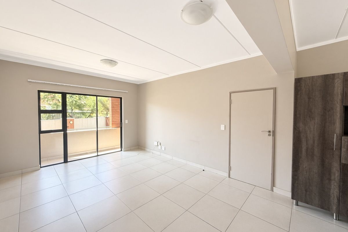Spacious, light-filled living area featuring neutral tiled flooring, a sliding glass door leading to a balcony, and a built-in storage cupboard.