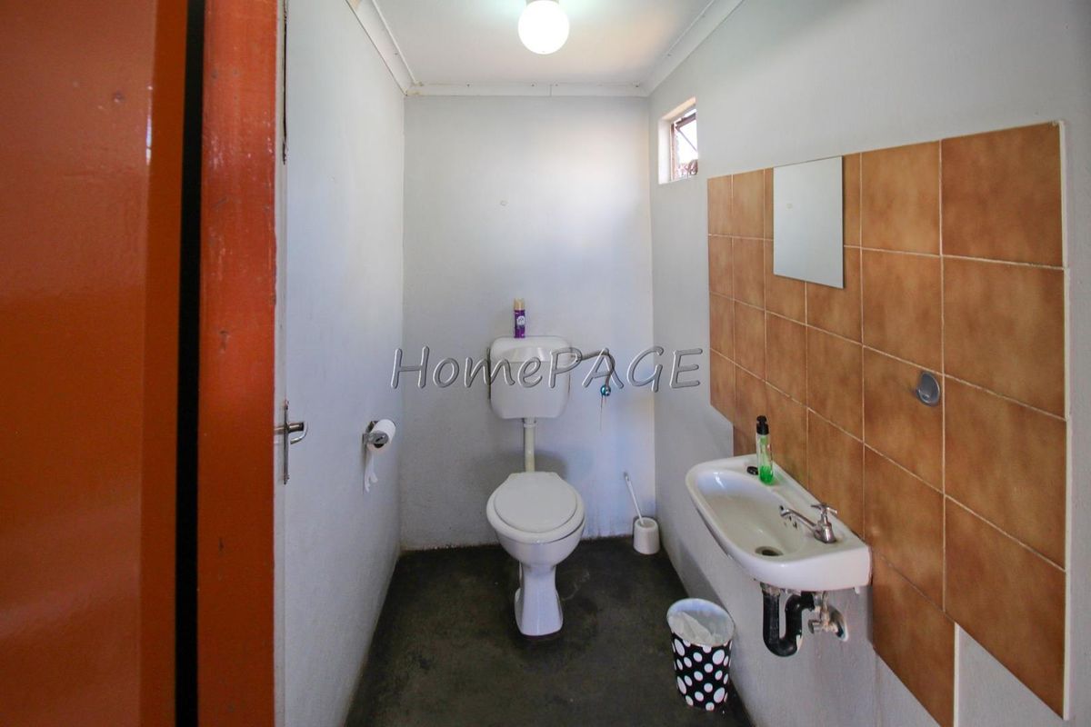A compact industrial-style restroom featuring a standard toilet, wall-mounted basin, and partial wall tiling.