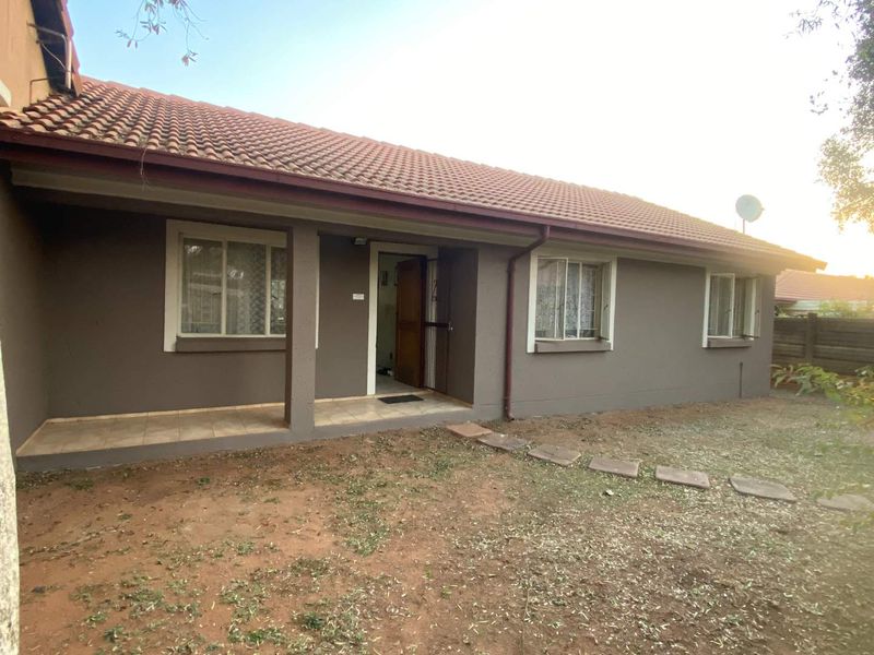 Front elevation of a townhouse featuring a covered patio, tiled roof, and security entrance gate, set against a modest garden area.