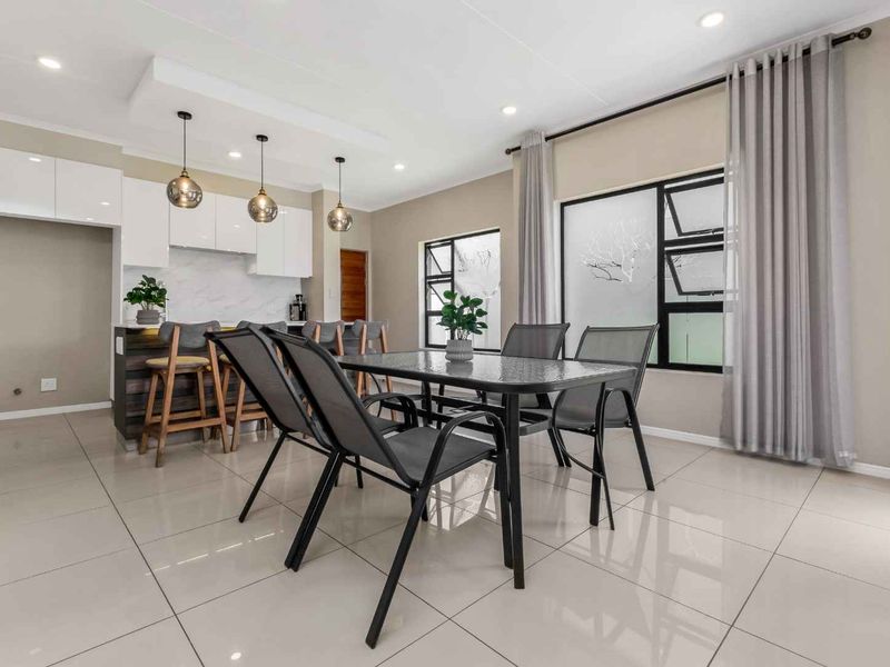 Modern open-plan living and dining area featuring sleek kitchen cabinetry, a central island, tiled flooring, and contemporary recessed and pendant lighting.