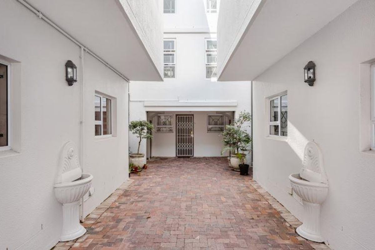 A well-maintained exterior courtyard featuring brick paving, wall-mounted lanterns, and decorative pedestal water features between apartment building wings.