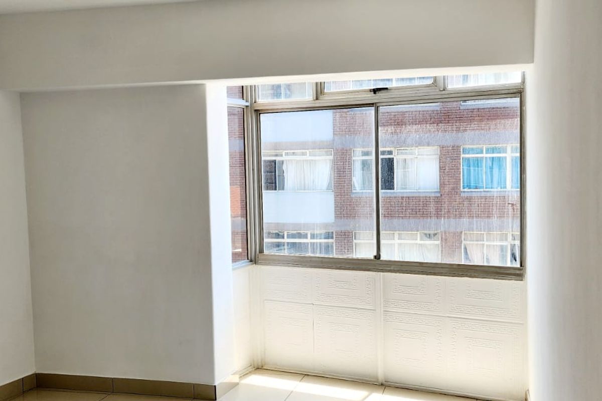 An empty bedroom featuring tiled flooring and a large window with views of the neighboring building.