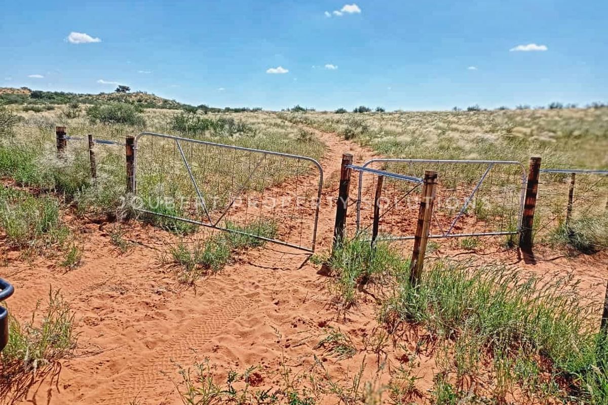 A rural farm access point featuring a metal gate and wooden fencing set within a natural, open landscape.