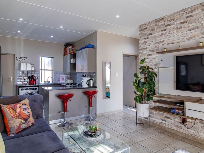 Open-plan living area featuring a modern kitchen with breakfast bar, tiled flooring, and a stone-clad feature wall with integrated media storage.