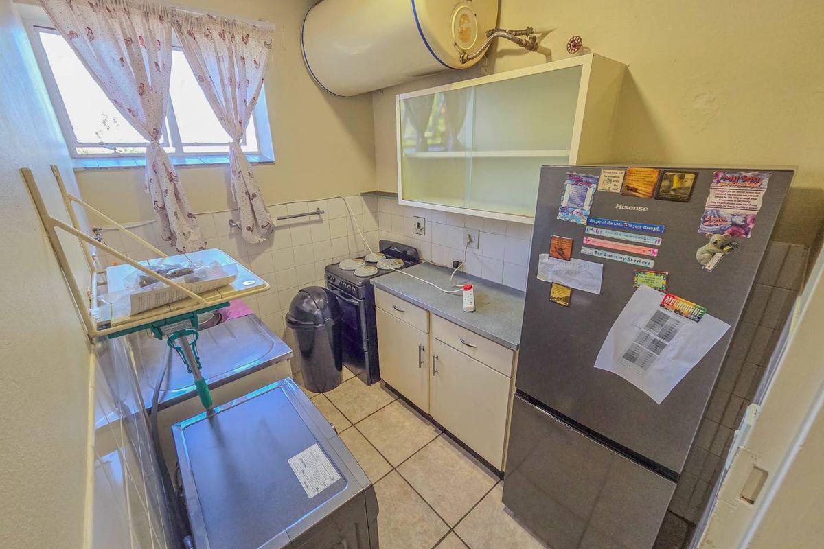 Compact kitchen featuring tiled flooring, built-in cabinetry, a stainless steel sink, and a wall-mounted electric water heater.