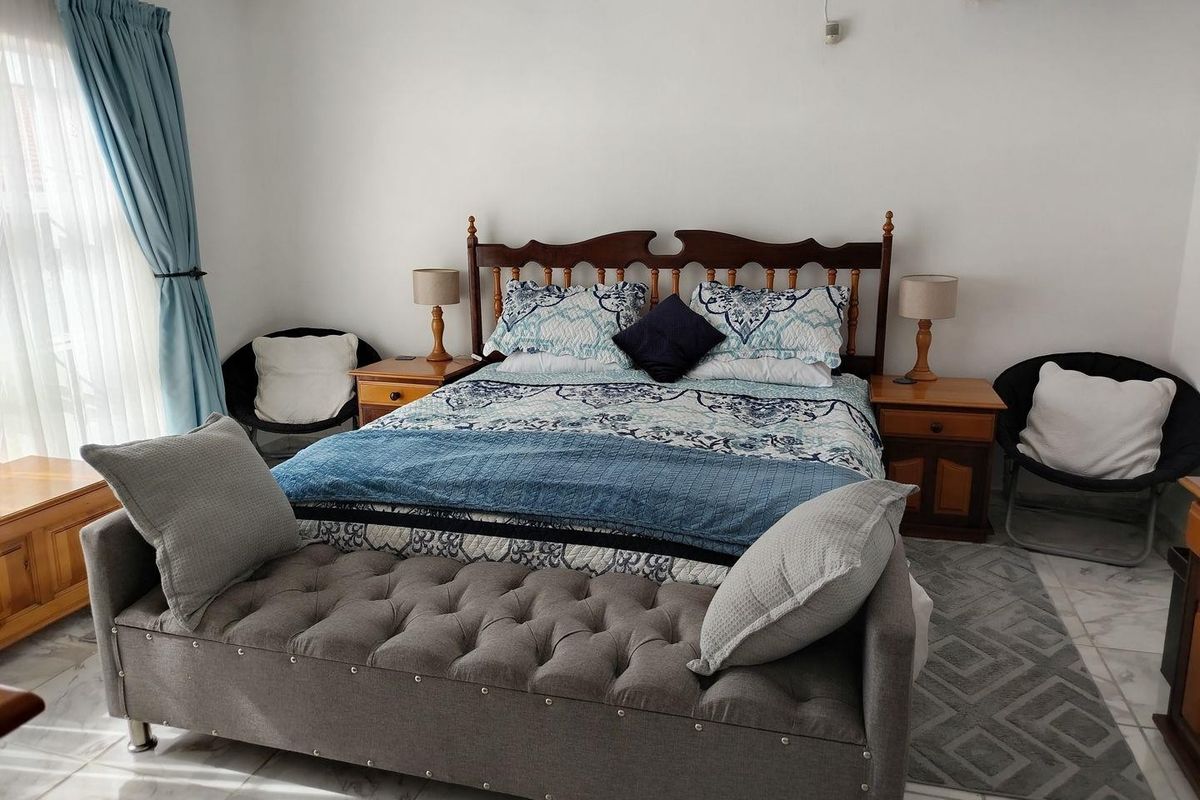 A well-lit bedroom featuring tiled flooring, a wall-mounted air conditioning unit, and large windows with curtains.