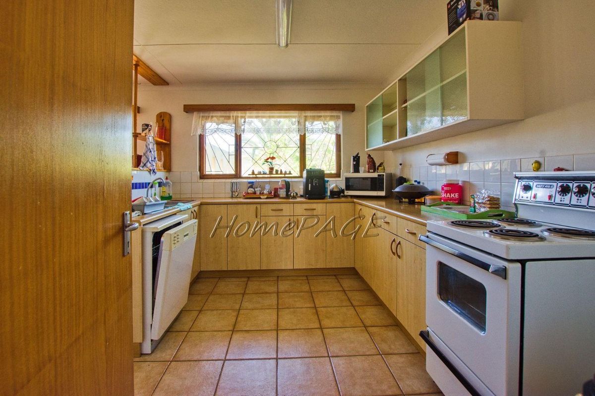 A functional kitchen featuring light wood-finish cabinetry, tiled flooring, a built-in stove, and a window overlooking the exterior.