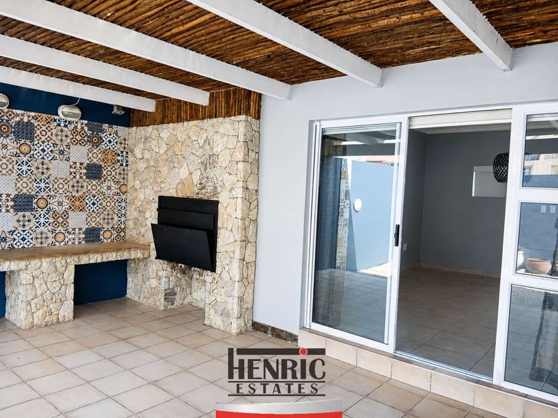 Covered patio featuring a built-in braai, stone cladding, decorative tile accents, and sliding glass doors leading into the interior living space.