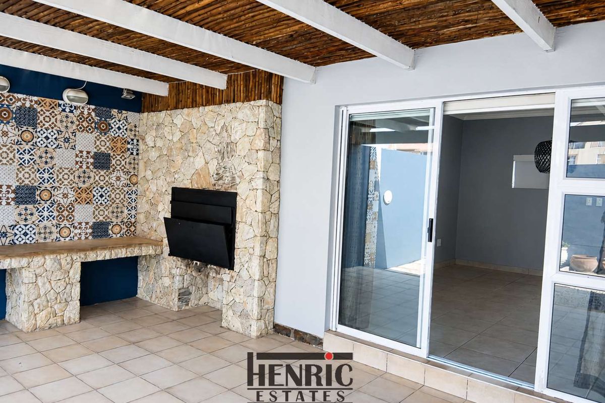 Covered patio featuring a built-in braai, stone cladding, decorative tile accents, and sliding glass doors leading into the interior living space.