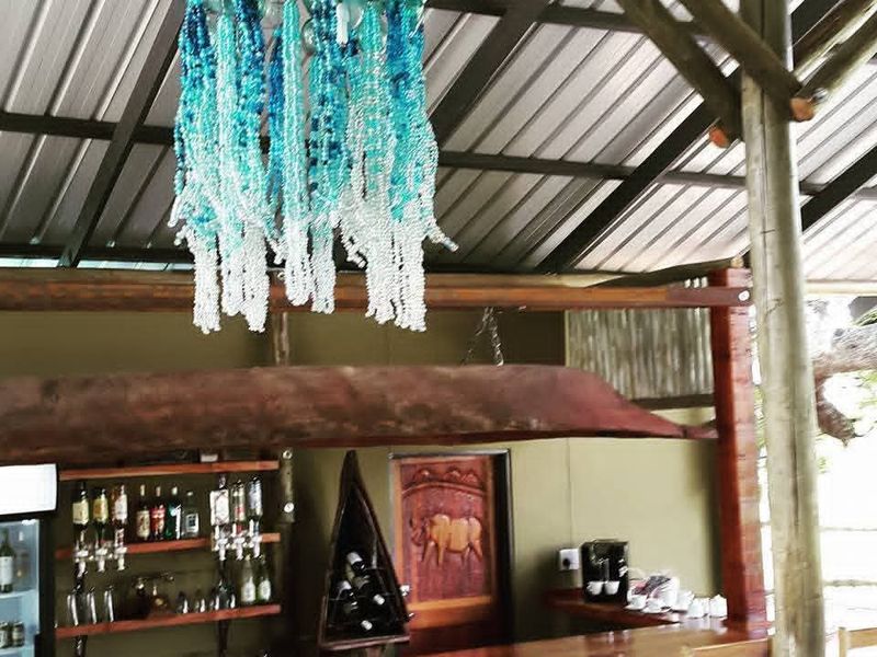 Rustic bar area featuring a wooden counter, exposed timber roof beams, and corrugated metal roofing, creating a warm and authentic guest house atmosphere.