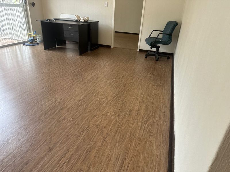 A functional office space featuring durable laminate flooring and a secure entrance gate, offering a clean and versatile area for work or study.