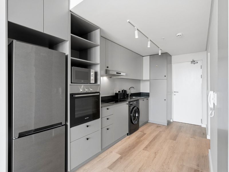 Modern, compact kitchen featuring sleek grey cabinetry, integrated appliances, built-in oven, microwave, and durable laminate flooring in a clean, contemporary layout.