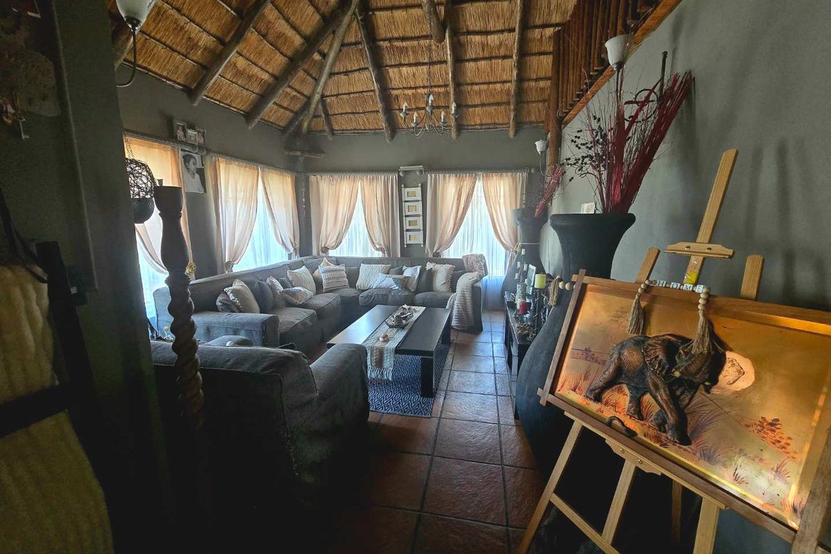 Spacious living room featuring a high vaulted thatched ceiling with exposed timber rafters and traditional terracotta floor tiles.