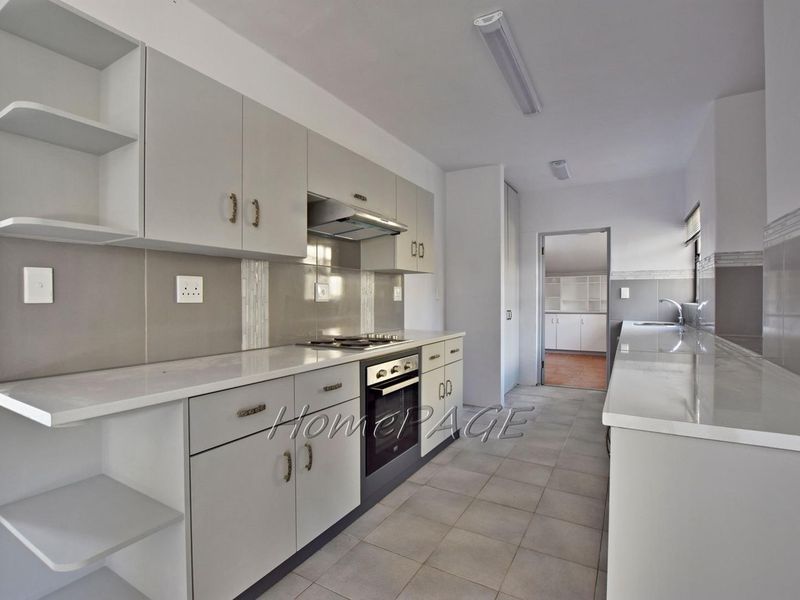 A clean, modern kitchen featuring light grey cabinetry, stone countertops, built-in oven, gas hob, and tiled flooring with a neutral color palette.