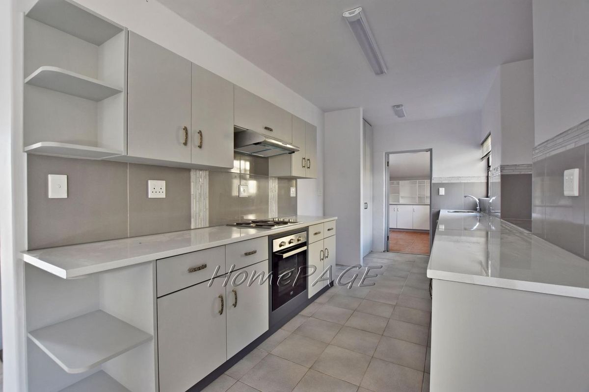 A clean, modern kitchen featuring light grey cabinetry, stone countertops, built-in oven, gas hob, and tiled flooring with a neutral color palette.