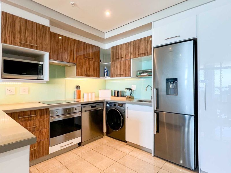 Modern kitchen featuring high-gloss wood-grain cabinetry, stone countertops, glass splashback, and integrated stainless steel appliances including an oven, hob, and dishwasher.