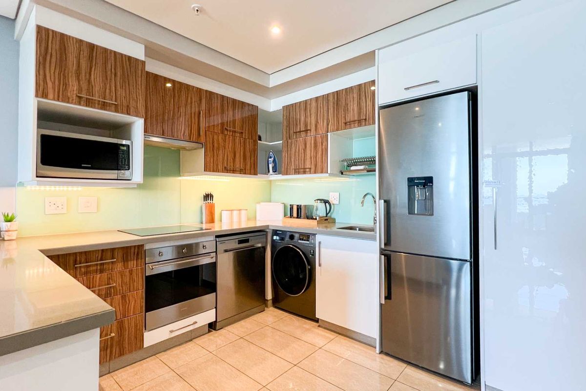 Modern kitchen featuring high-gloss wood-grain cabinetry, stone countertops, glass splashback, and integrated stainless steel appliances including an oven, hob, and dishwasher.
