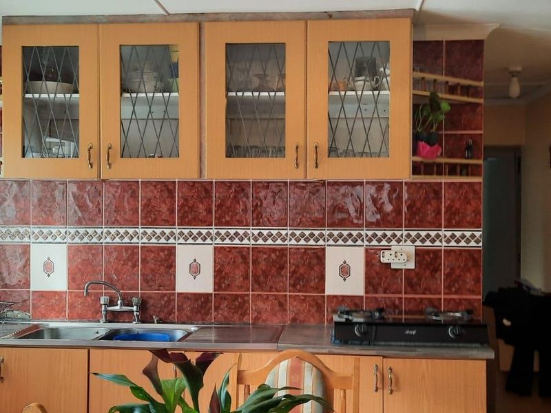 A functional kitchen featuring wood-tone cabinetry, a stainless steel sink, and a gas hob set against a distinctive tiled backsplash.