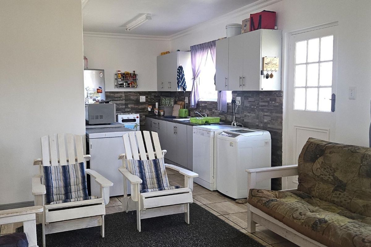 A functional kitchen area featuring built-in cabinetry, tiled splashbacks, and integrated laundry appliance connections, adjacent to a casual living space.
