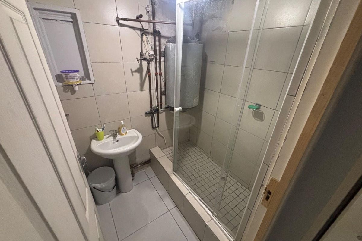 Compact bathroom featuring a pedestal basin, a glass-enclosed shower, and exposed water heating infrastructure.
