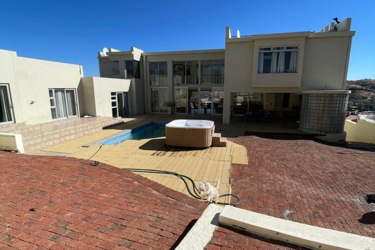 Rear exterior view featuring a swimming pool, built-in spa, timber decking, and extensive brick paved patio area with large glass sliding doors.