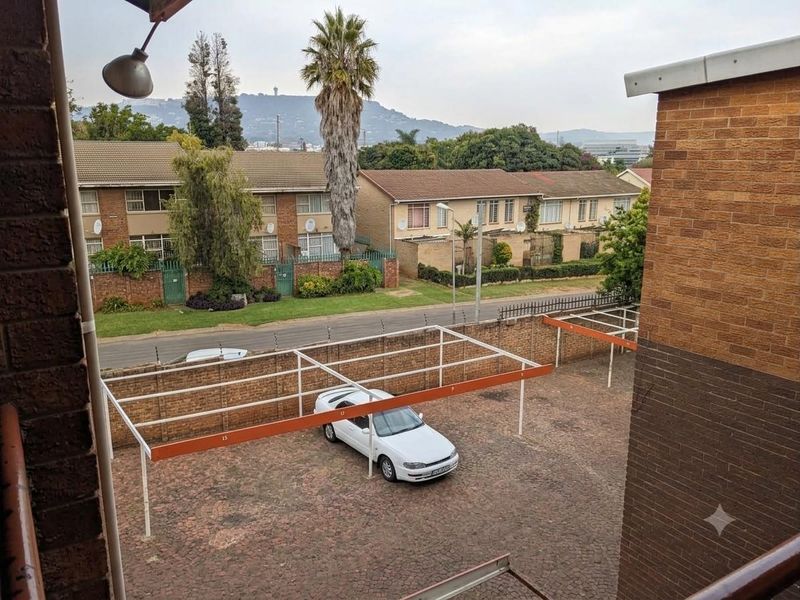 Elevated view overlooking the apartment complex parking area, featuring paved surfaces, carport structures, and perimeter brick walling with electric fencing.