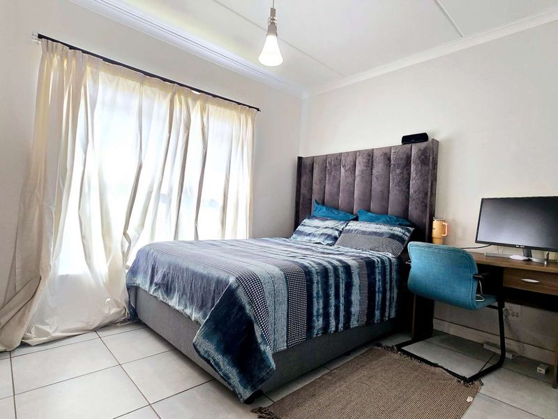 A well-lit bedroom featuring neutral tiled flooring, ceiling cornice detailing, and a large window with curtain treatments.
