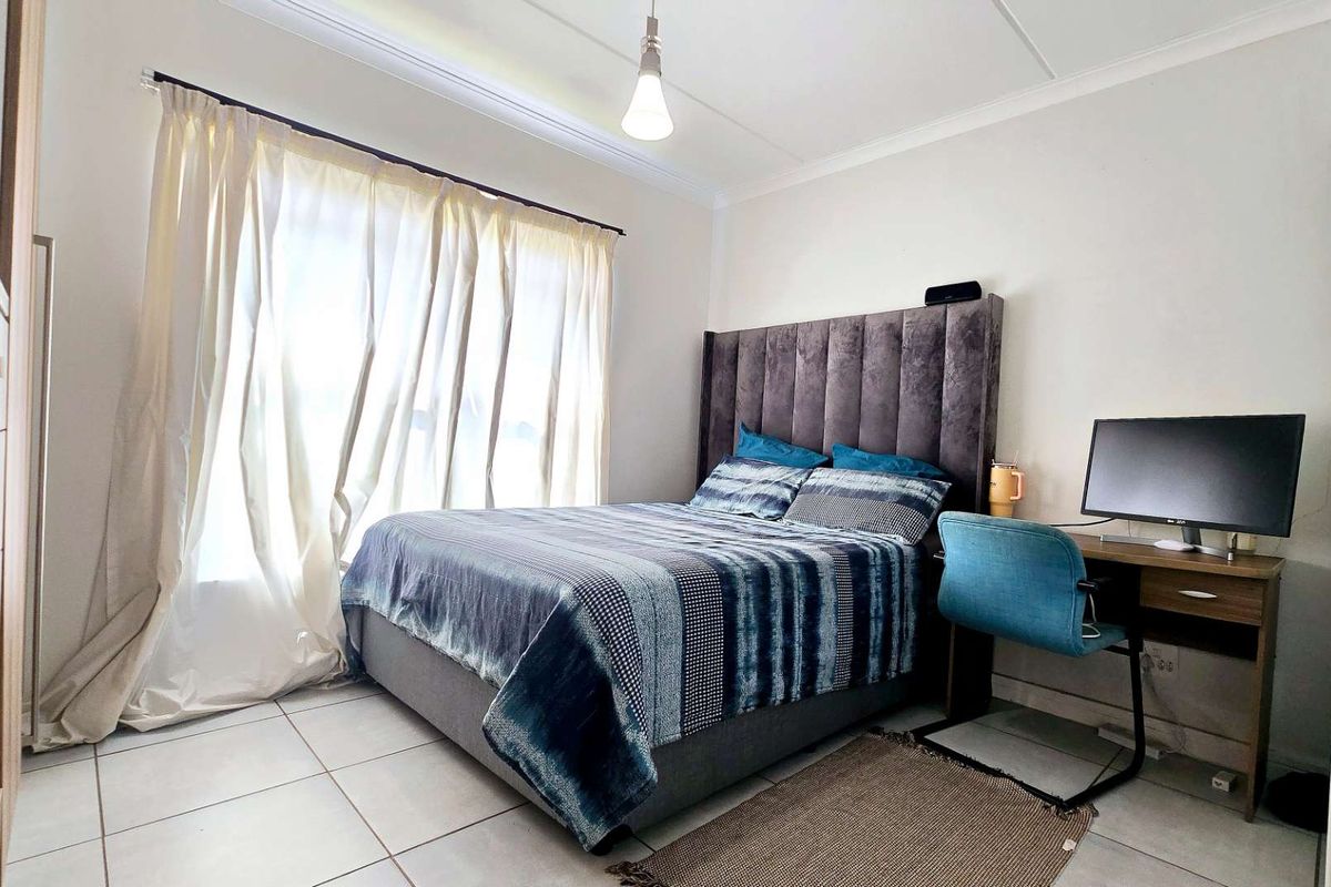 A well-lit bedroom featuring neutral tiled flooring, ceiling cornice detailing, and a large window with curtain treatments.