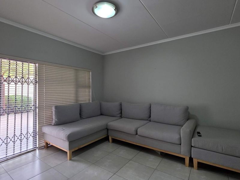 A living room featuring neutral grey walls, tiled flooring, and a sliding glass door with security gate and venetian blinds.
