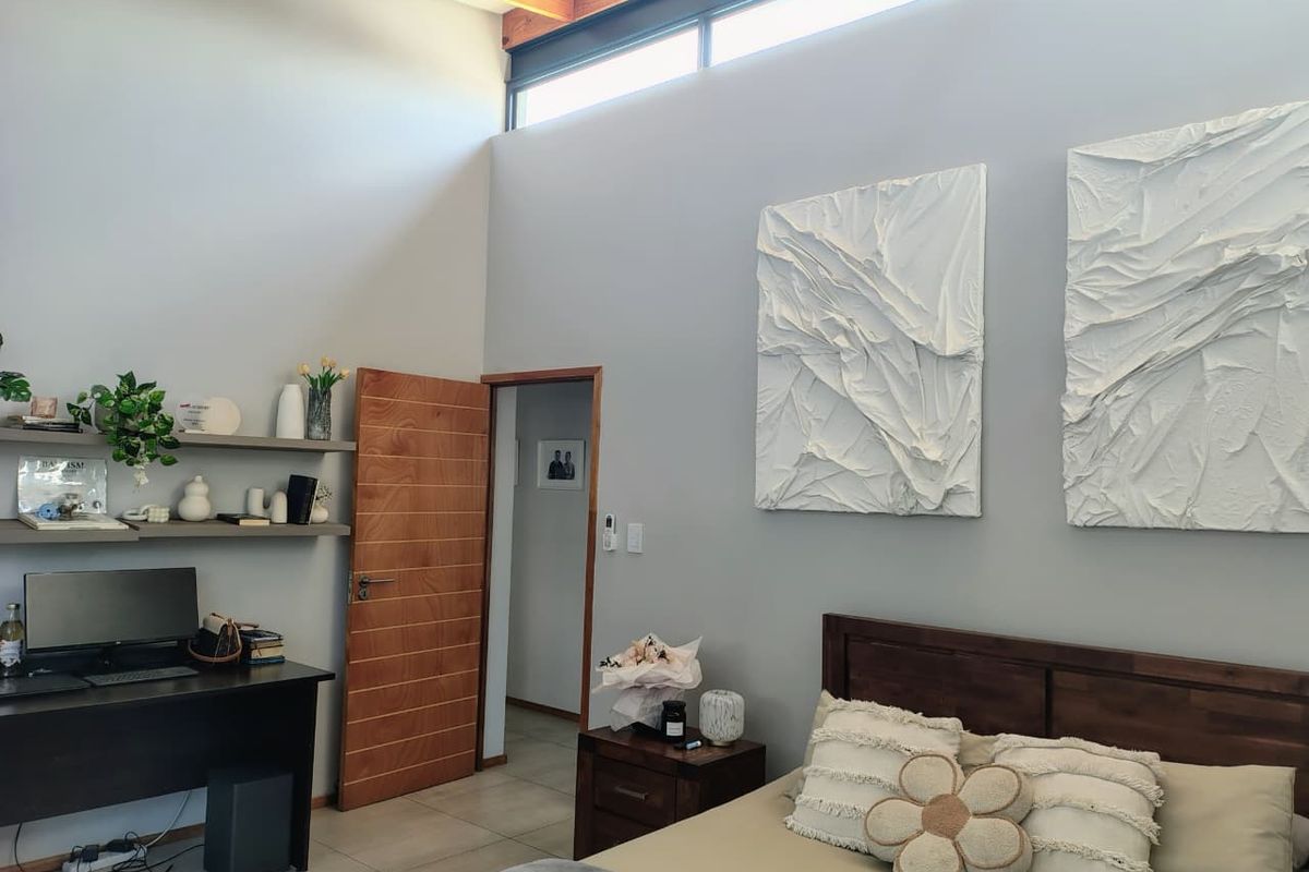 Spacious bedroom featuring high vaulted ceilings with exposed timber beams, clerestory windows, tiled flooring, and a solid timber door.