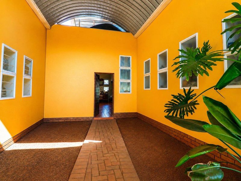 A covered outdoor patio area featuring a distinctive curved metal roof, brick paved walkway, and bright yellow walls with multiple casement windows.