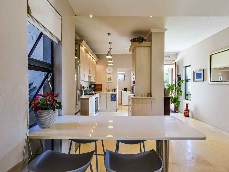 Open-plan kitchen area featuring neutral cabinetry, integrated appliances, and tiled flooring, flowing into a bright living space with modern finishes.