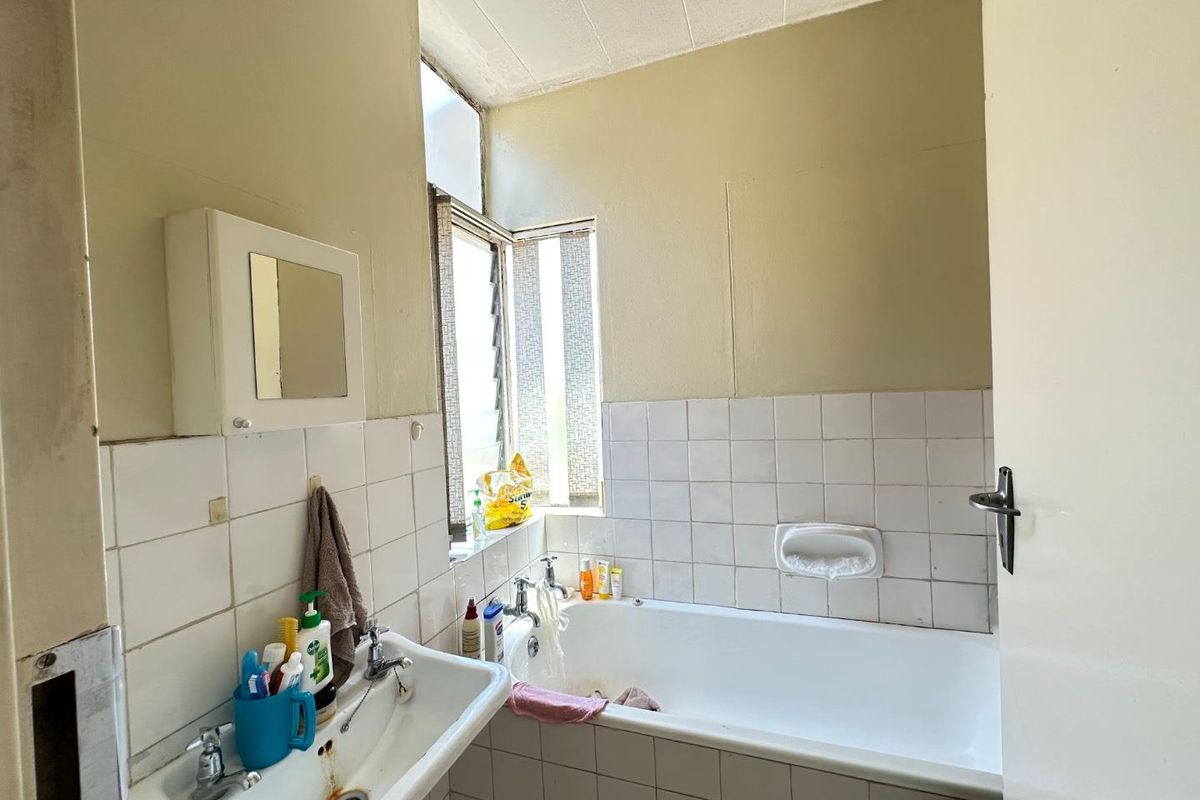 A dated bathroom featuring a standard bathtub, wall-mounted basin, and tiled splashbacks, requiring cosmetic updates and maintenance.